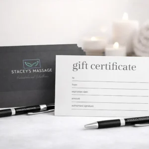 Stacey’s Massage gift certificates displayed on a clean spa-style surface, featuring dark grey branded envelopes, white gift vouchers, and branded pens.